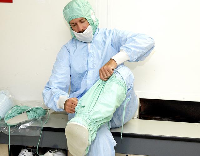 A Kennedy Space Center employee dons the foot and leg covers of a "bunny suit," part of standard clean room apparel, before entering a clean room. Photo: NASA